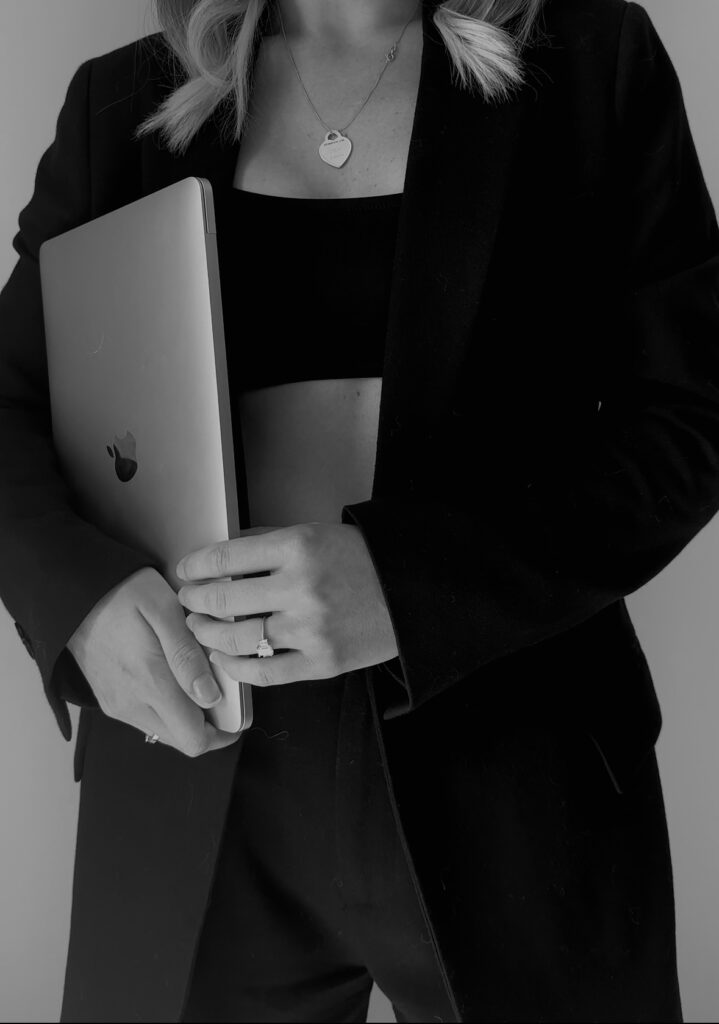 Black and white photo for a girl in a pantsuit with a crop top underneath holding a macbook pro.